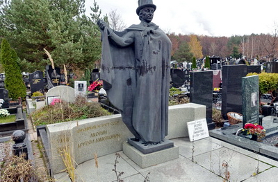 Статуя человека в шляпе перед широким надгробьем